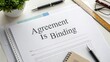 © Syawal - Document with the phrase 'Agreement Is Binding' emphasizing legal commitment on a desk with office supplies and a plant