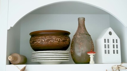 Clay pot, stack of plates, bottle, ceramic house, wooden object on shelf