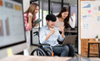 © NAMPIX - A diverse team of young professionals, including a man in a wheelchair, celebrates their success with joy and excitement while looking at a laptop in a office.