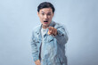 © Daniel - Asian man in denim jacket pointing finger directly at camera with serious face, standing in studio against plain light background, showing accusation, warning, and commanding gesture