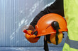 © vadish - Worker holding orange safety helmet with protective earmuffs for construction and industry. Industrial safety, construction equipment, and protective workwear against noise and hazards.