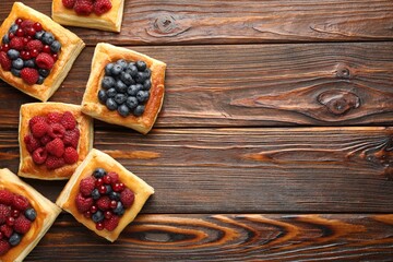 Wall Mural - Tasty puff pastries with berries on wooden table, flat lay. Space for text