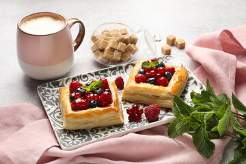 Wall Mural - Tasty puff pastries with berries, mint, brown sugar and coffee on light grey table, closeup