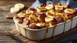 © fivan - Banana bread pudding in baking dish, warm autumn lighting, scattered banana slices and caramel swirls, vintage wood table, open space on side