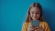 © maxximmm - Smiling girl holding cell phone. Young girl smiles on phone in 4k video. Field of vibrant blue with a shallow blue backdrop. A girl with a smile is holding lifestyle a mobile phone.