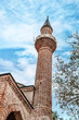 The towering minaret of Suleymaniye Mosque in Alanya, Turkey, reaching into the blue sky. This historic Ottoman structure features traditional brickwork and intricate design elements