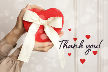 Wall Mural - Thank you card design with gift box in woman's hands against white wall. Bokeh effect