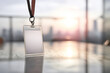 © Kowit - A plain ID badge hangs on a lanyard, placed on a reflective surface with a blurred cityscape in the background, suggesting a professional or event context.