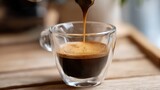 Fresh espresso pouring into a clear glass cup on a wooden table