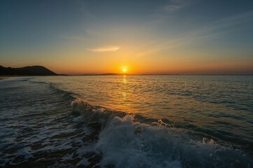 Wall Mural - distant perspective of a seaside at dusk, featuring warm orange and golden hues and gentle vertical 