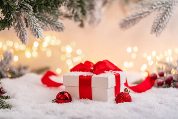 Wall Mural - white gift box with red ribbon and ornaments under snowy branches, set against warm holiday lights. 