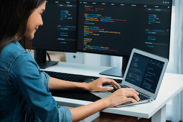 Smiling young Asian in IT developer creating with typing online information on laptop with coding program data of application, wearing jeans shirt. surrounded by safety analysis two screen. Stratagem.