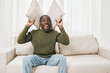 © SHOTPRIME STUDIO - Happy man expressing joy with pillows in a modern living room, wearing cozy sweater and jeans, against a bright and airy background