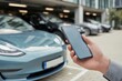 © MUHAMADFADZLAN - Person Using Smartphone to Connect with Electric Vehicle Technology