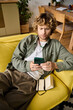 © LIGHTFIELD STUDIOS - Stylish man relaxing on yellow couch while using smartphone in modern living space