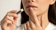 © MUHAMMAD - Close-up of a young woman applying moisturizing lip balm for healthy and hydrated lip care