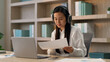 © Yuliia - Asian Chinese woman female office worker girl Japanese Korean businesswoman teacher tutor work in wireless headphones talking online laptop video call business meeting discuss report document indoors