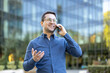 © Liubomir - Happy business man making a phone call, standing outdoors in front of a modern office building, representing urban communication and professional networking