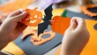 © Enigma - Child hands holding and assembling halloween garland with diy paper pumpkin, bat, and jack o'lantern decorations, creating festive crafts for the holiday celebration