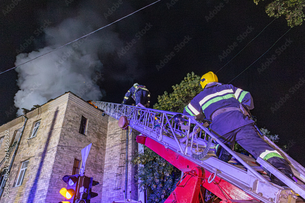 Firefighters extinguishing a burning building at night using a ladder ...