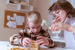 © looking2thesky - A mother and her son with hearing aids share a joyful moment playing board games together. A heartwarming scene of inclusive family bonding, love, and adaptive play