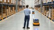 © Johnnii - A worker observes automated robots in a modern warehouse filled with neatly stacked boxes, highlighting advancements in logistics technology.