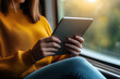 © SnapVault - Woman in yellow sweater sits by train window holding a tablet, reading and browsing during commute, relaxed, connected, enjoying daylight travel and digital leisure on the go
