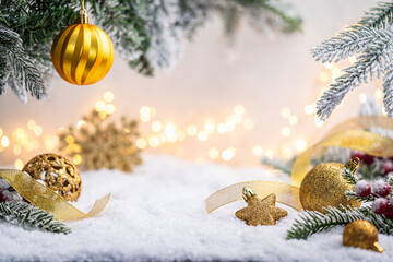 Wall Mural - glittering gold ornaments and snowflakes rest on snowy ground with frosted pine branches and soft gl