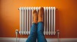 © Alchemy - Person in knitted orange socks resting feet on white radiator against bright orange wall, symbol of winter heating, cozy home atmosphere, warmth, comfort, relaxation and energy efficiency
