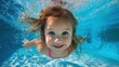 © mila103 - A cheerful young girl with bright blue eyes swims underwater smiling widely. The sunlight creates a vibrant blue hue in the pool showcasing her playful spirit.