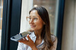 © Yaroslav Astakhov - A professional woman is actively engaged in a conversation while using her smartphone near a large window