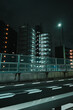 A modern building with illuminated windows stands against a dark night sky, as streetlights glow over a highway with white road markings.
