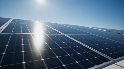 Close-up of a solar panel array under a clear blue sky with bright sunlight reflecting off