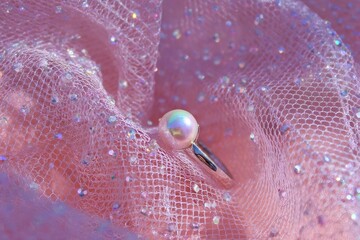 Iridescent pearl ring rests on pink tulle