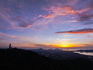 Wall Mural - Arial view stunning sunrise above Phuket big Buddha on the mountain. A breathtaking panoramic view of a vibrant sunrise casting warm hues over a coastal town, with the sea reflecting of the sky