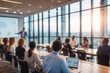 © Olivia - Modern corporate training session in a bright glass-walled conference room. A group of young professionals attentively listens to a speaker presenting slides with charts on a large projector screen