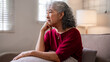 © snowing12 - Asian older woman sits on sofa thinking alone quiet home peaceful moment senior living room contemplative mood looking window retirement thoughts