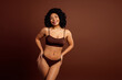 © deagreez - Confident woman in stylish lingerie posing against brown background, showcasing body positivity and natural beauty
