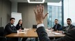© Rajab - A man raises his hand in a business meeting with colleagues seated around a conference table.