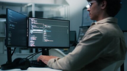 Focused Male IT Programmer working in software developing office, Writing code using desktop computer review and analysis data on monitor screen developing a new software app development project.