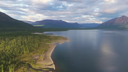 Golden evening light paints Lake Lama and a quiet headland. Calm water reflects cloud and mountain. Remote Putorana Plateau in Russia, rare access, ideal for travel, nature, and documentary use