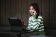 © Worawi - A young woman wearing headphones works on a laptop at a café table, smiling and focused, with a coffee cup beside her.