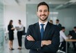 © sujon1638 - Confident business professional poses with arms crossed in a modern office environment with colleagues blurred in background