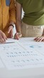© rogerphoto - Two business professionals are collaborating on a project, analyzing financial charts and statistics displayed on a table, using a calculator for precise calculations. close up vertical view