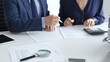 © rogerphoto - Close up of magnifying glass and calculator over financial documents opposite financial team, reviewing reports, collaborating on accounting details at modern office workspace. Audit and taxes