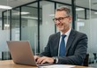 © sujon1638 - Smiling businessman in a modern office environment typing on a laptop computer with a professional demeanor