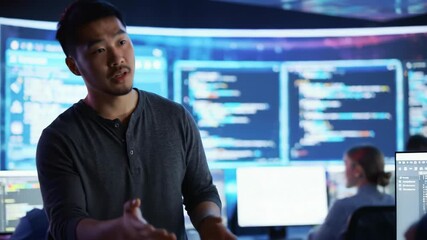 Asian man software engineer working in a team at computer, with code on screen. Technology, development, programmer, coding, and software are central themes.