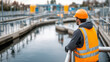 © Ramses - A diligent worker in an orange safety vest and yellow hard hat oversees wastewater treatment basins from a viewing deck, ensuring smooth operation and safety in an industrial water facility.