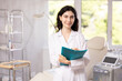 © JackF - Smiling woman doctor in uniform standing in clinic, filling out clipboard with medical records