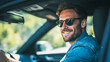 © Daria - Smiling man wearing sunglasses and denim jacket enjoying a sunny day while driving a car surrounded by lush green outdoor scenery viewed through the side window